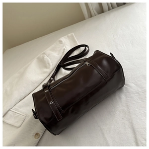 Detail einer dunkelbraunen zylindrischen Boston Bag aus glänzendem Leder auf Stoff