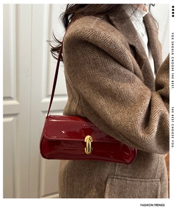 Detail of red patent leather shoulder bag with gold twist lock on brown wool coat
