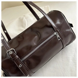 Detailed view of glossy dark brown barrel bag with vintage leather texture and silver zipper
