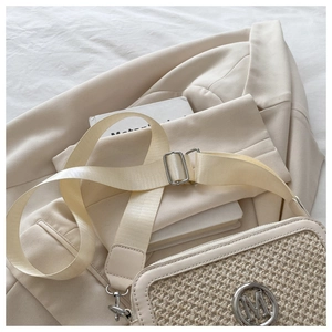 Detail of woven beige shoulder bag featuring a circular metal M logo and wide strap