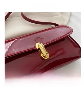Detail view of red patent leather shoulder bag with elegant gold metal buckle closure