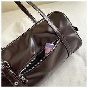 Detail of dark brown glossy shoulder bag showing a side zipper pocket with small bottle