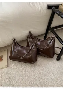 Dettaglio borsa sottobraccio in pelle marrone scuro con catena e finitura lucida