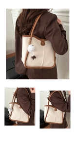 Detail of cream tote bag with brown leather trim and plush ball charms on strap