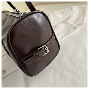Detail of dark brown cylindrical shoulder bag featuring silver metal buckle and premium texture