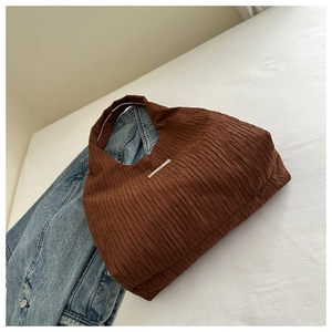 Détail d'un sac cabas plissé marron avec une étiquette argentée sur fond blanc