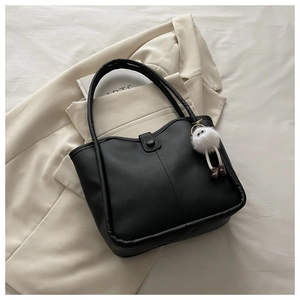 Detail of black leather tote bag featuring a round buckle and white plush monster charm