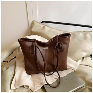 Detail of deep brown tote bag in pebbled leather with metallic logo plate on blazer