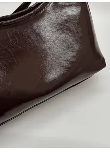 Detail of glossy brown faux leather handbag showing oily texture and printed text