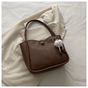 Close-up of deep brown leather tote bag with vertical stitching and plush charm detail