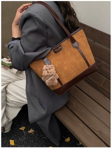 Detail of a large tote bag with embossed cat design and a plush bear charm on a park bench