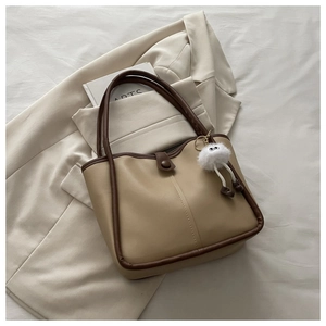 Close-up of beige tote bag with brown trim and cute plush monster charm detail
