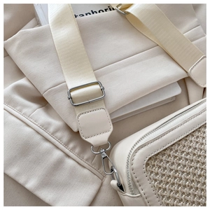 Detail of cream crossbody bag featuring woven panels and wide nylon shoulder strap with metal clips