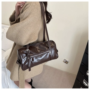 Detail of dark brown cylindrical crossbody bag with silver buckles and leather texture