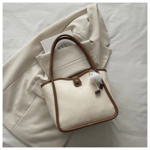 Detail of cream tote bag with brown trim, vertical stitching and cute plush pendant charm