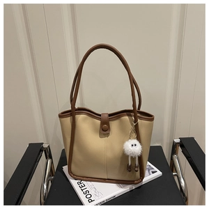 Detail of a beige PU leather tote bag with dark brown handles and cute monster charm
