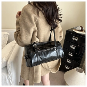 Close-up of a glossy black cylinder bag with silver hardware on a wool coat