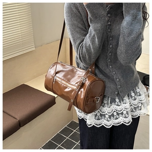 Detail view of the brown leather barrel bag with metal eyelets and zipper closure