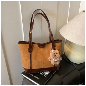 Detail of camel suede tote bag with embossed cat design and plush bear charm decoration
