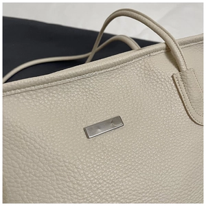 Close-up of beige lychee grain leather tote bag featuring a polished silver metal plate