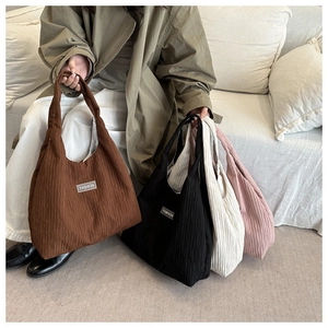 Pleated tote bags in brown, black, white, and pink displayed on a cozy sofa