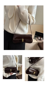 Detail view of glossy dark brown leather shoulder bag with gold oval metal clasp closure