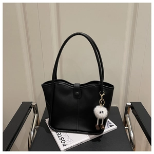 Detail of black faux leather tote bag with fluffy white monster pendant on a chair
