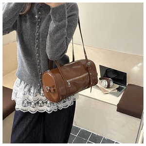 Brown leather cylinder shoulder bag with silver rivet details shown in lifestyle setting