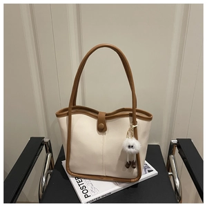 Detail of off-white canvas tote bag with brown leather trim and plush monster charm