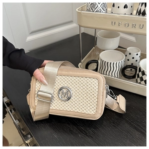 Detail of beige woven crossbody bag with metallic M logo and wide fabric shoulder strap