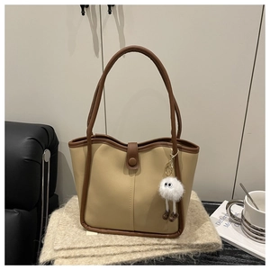 Detail of khaki tote bag with dark trim, magnetic snap, and plush doll charm
