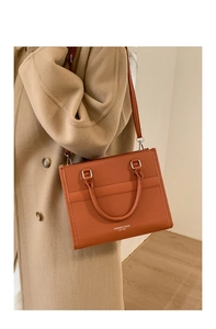 Borsa a tracolla alla moda in pelle arancione su un cappotto di lana color cammello in interni