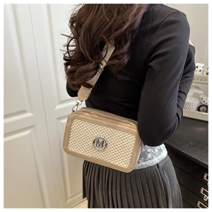 Detail of beige woven crossbody bag with metal M logo and wide strap worn by model