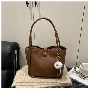 Detail of a brown PU leather tote bag with vertical stitching and cute plush pendant