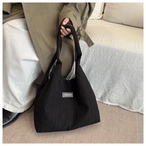 Detail of black pleated texture handbag featuring a fashion fabric label on the front