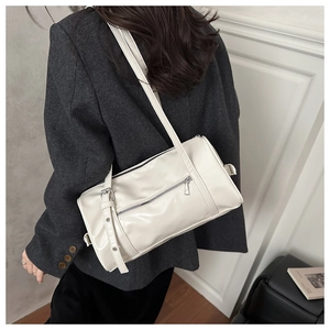 Detail of a creamy white cylindrical shoulder bag with silver metal buckle on leather strap