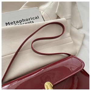 Close-up of wine red patent leather shoulder bag with glossy finish and metal twist lock
