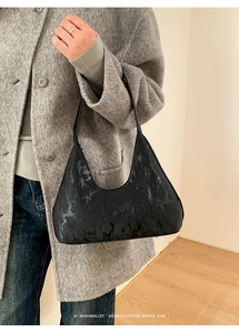 Dettaglio della borsa sottobraccio nera minimalista con trama retrò su sfondo di cappotto grigio