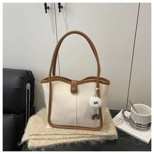 Detail of cream tote bag with brown leather trim and fluffy charm on a cozy blanket