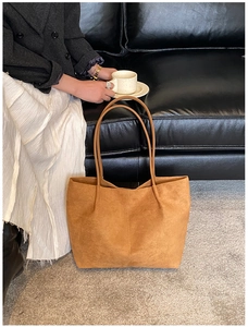 Detail of a large brown suede tote bag with central stitching on a textured floor