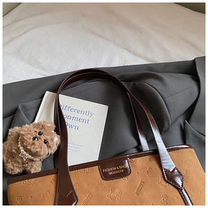 Detail of brown tote bag with embossed cat patterns and a small plush dog charm