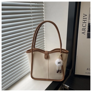 Detail shot of a minimalist cream tote bag with brown handles and plush eye charm