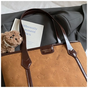 Detail of brown tote bag with embossed cat patterns and a cute plush puppy pendant charm