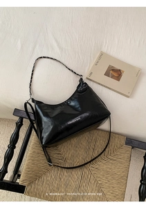 Detail of black glossy crescent bucket bag with metal chain and fashion text print