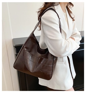 Detail of dark brown leather tote bag with grainy texture on a white suit model