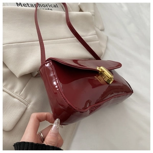 Detail of a dark red patent leather shoulder bag with gold twist-lock on a cream suit