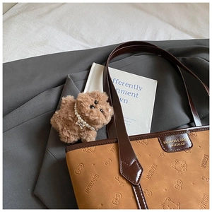 Detail view of brown tote bag with embossed cat patterns and plush teddy charm