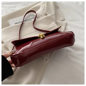 Detail of dark red patent leather shoulder bag with golden round metal twist lock