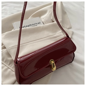 Detail of burgundy patent leather bag with gold clasp and textured flap on a book