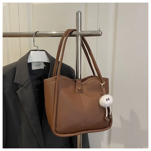 Close-up of brown tote bag with vertical stitching, snap button and plush eyeball charm